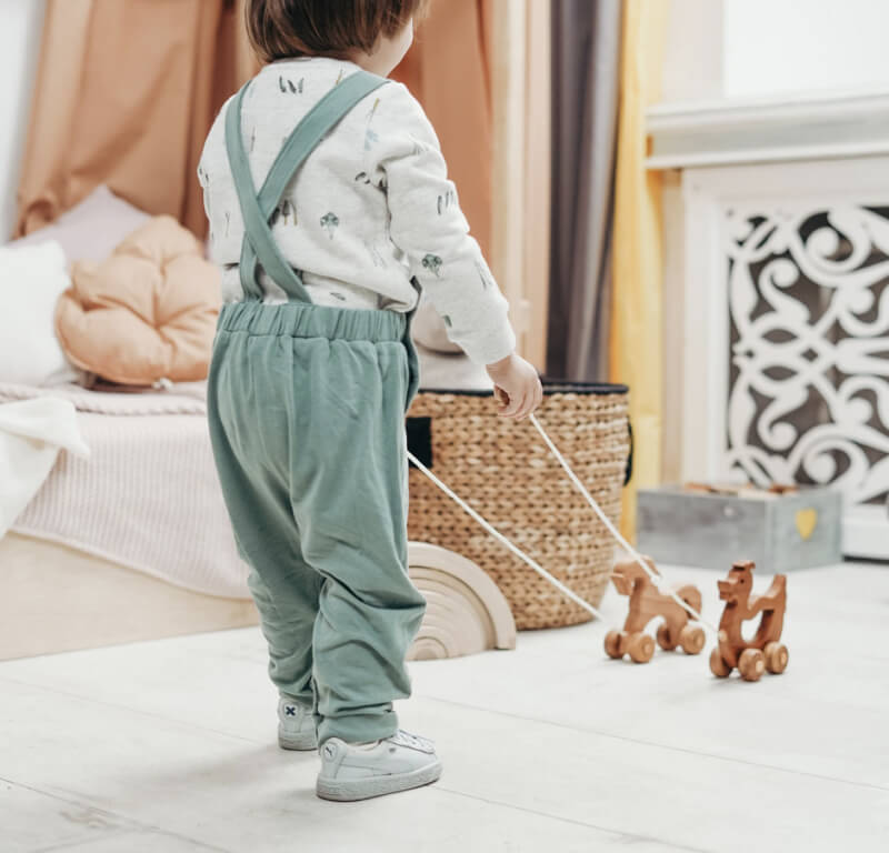 A toddler pulling two wooden animals on wheels